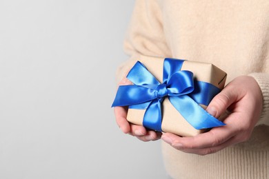 Photo of Woman holding gift box with blue bow on light grey background, closeup. Space for text