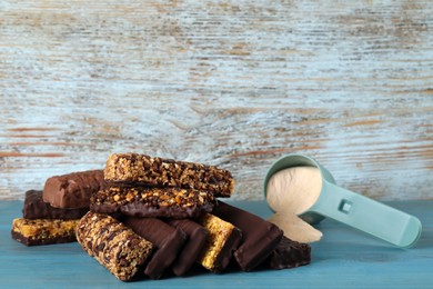 Photo of Different tasty bars and scoop of protein powder on light blue wooden table. Space for text