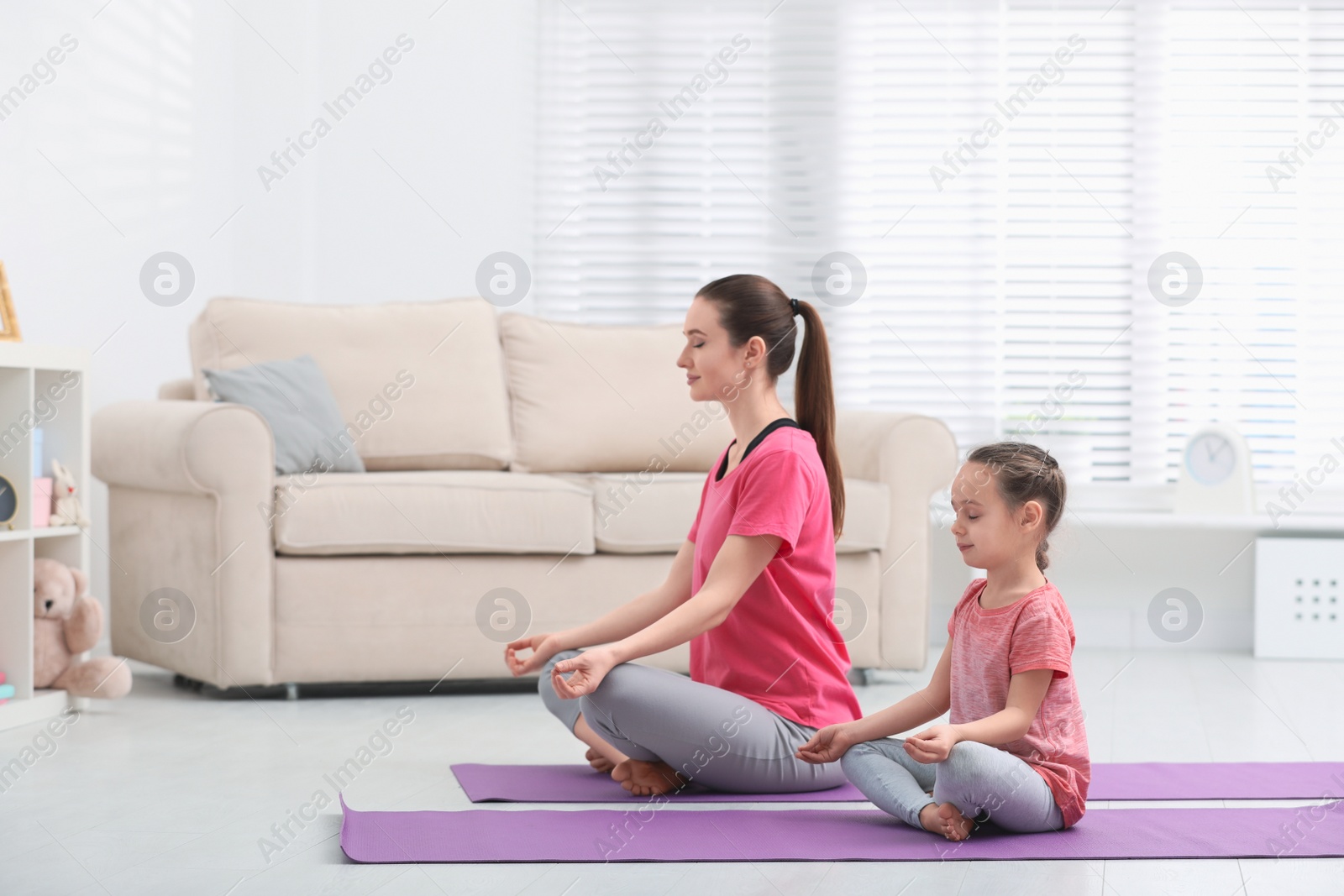 Photo of Young mother with little daughter practicing yoga at home