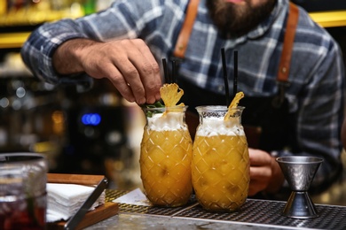 Photo of Bartender preparing tasty cocktail at counter in nightclub, closeup