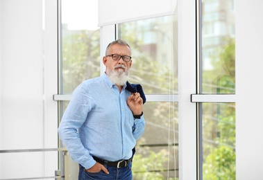 Portrait of handsome mature man with glasses and jacket near window