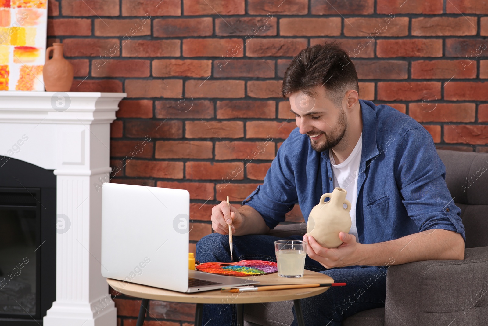 Photo of Happy man learning to decorate clay vase while watching online course at home. Time for hobby