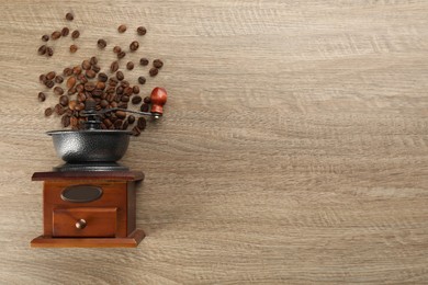 Photo of Vintage manual coffee grinder with beans on wooden table, flat lay. Space for text