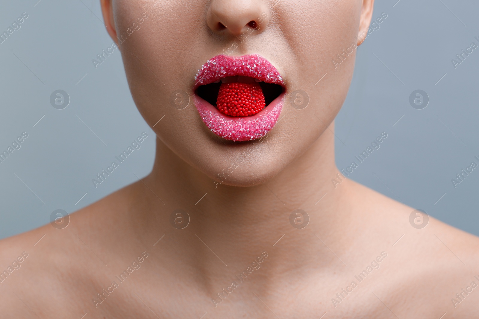 Photo of Woman with lips covered in sugar eating candy on light grey background, closeup