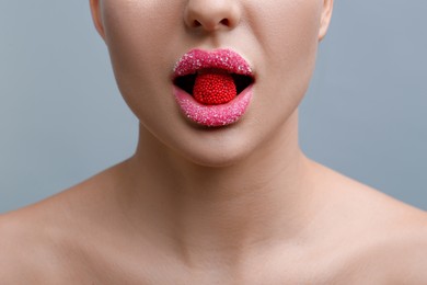 Photo of Woman with lips covered in sugar eating candy on light grey background, closeup