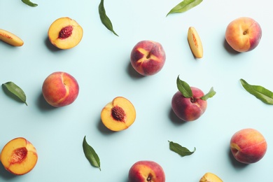 Photo of Fresh ripe peaches and green leaves on light blue background, flat lay