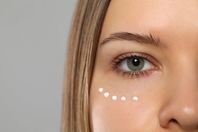 Young woman with cream around eye on light grey background, closeup. Space for text