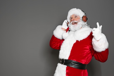 Santa Claus listening to Christmas music on color background