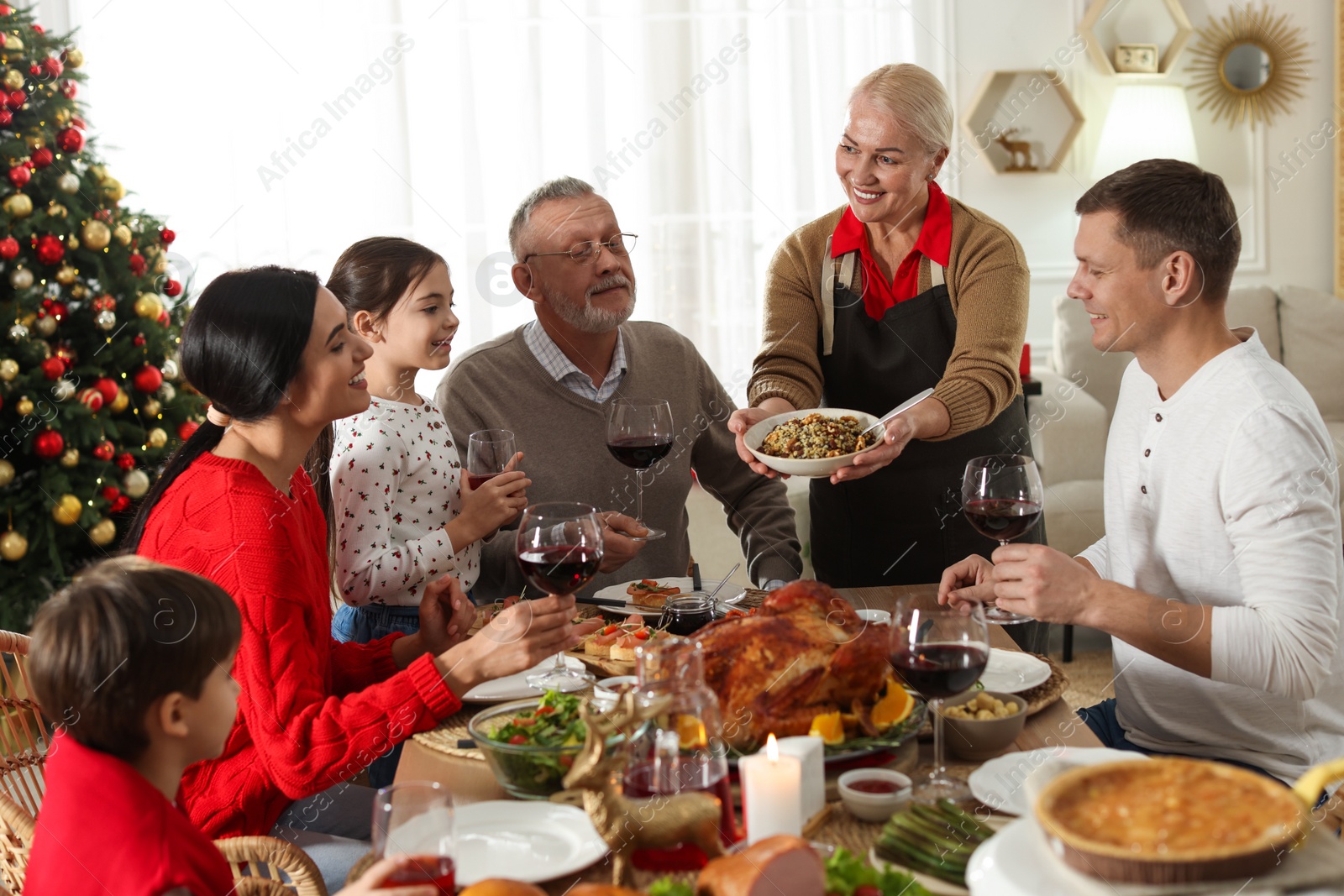 Photo of Woman with bowl of traditional Christmas kutia and her family during festive dinner at home. Slavic dish