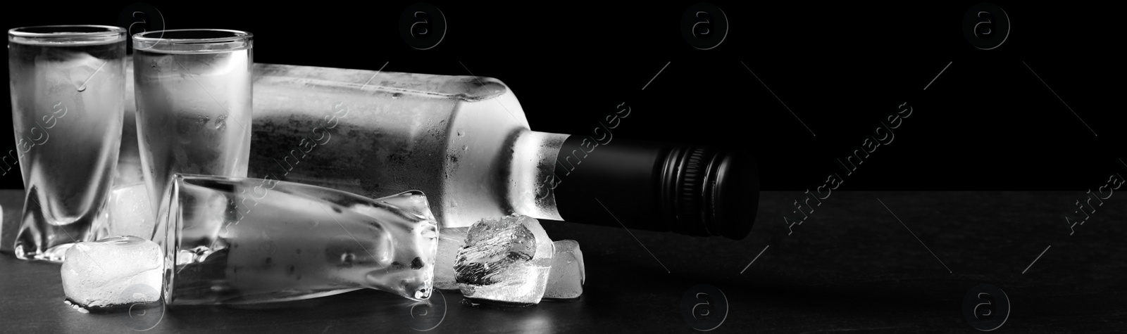 Image of Bottle of vodka and shot glasses with ice on table against black background, space for text. Banner design