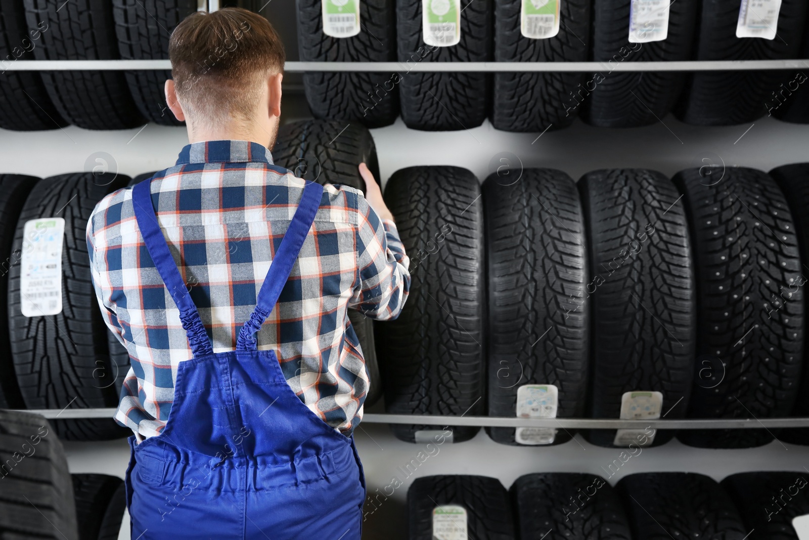 Photo of Young male mechanic with car tires in automobile service center