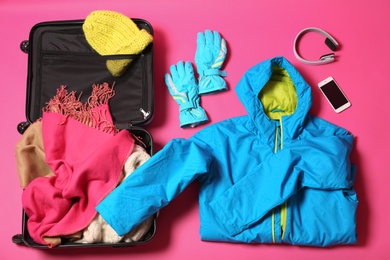 Flat lay composition with suitcase and warm clothes for winter vacation on color background