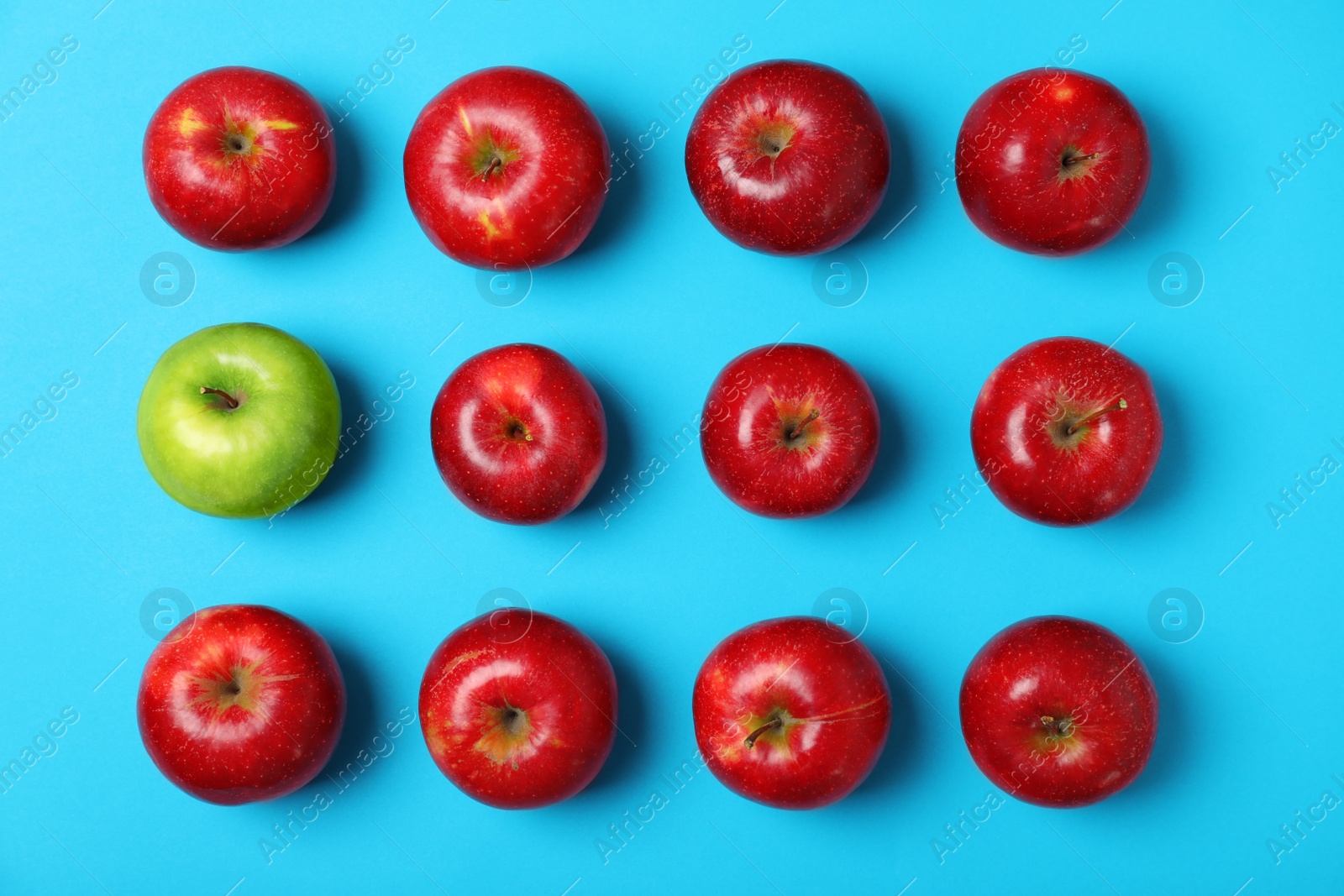 Photo of Green apple among red ones on color background, top view. Be different