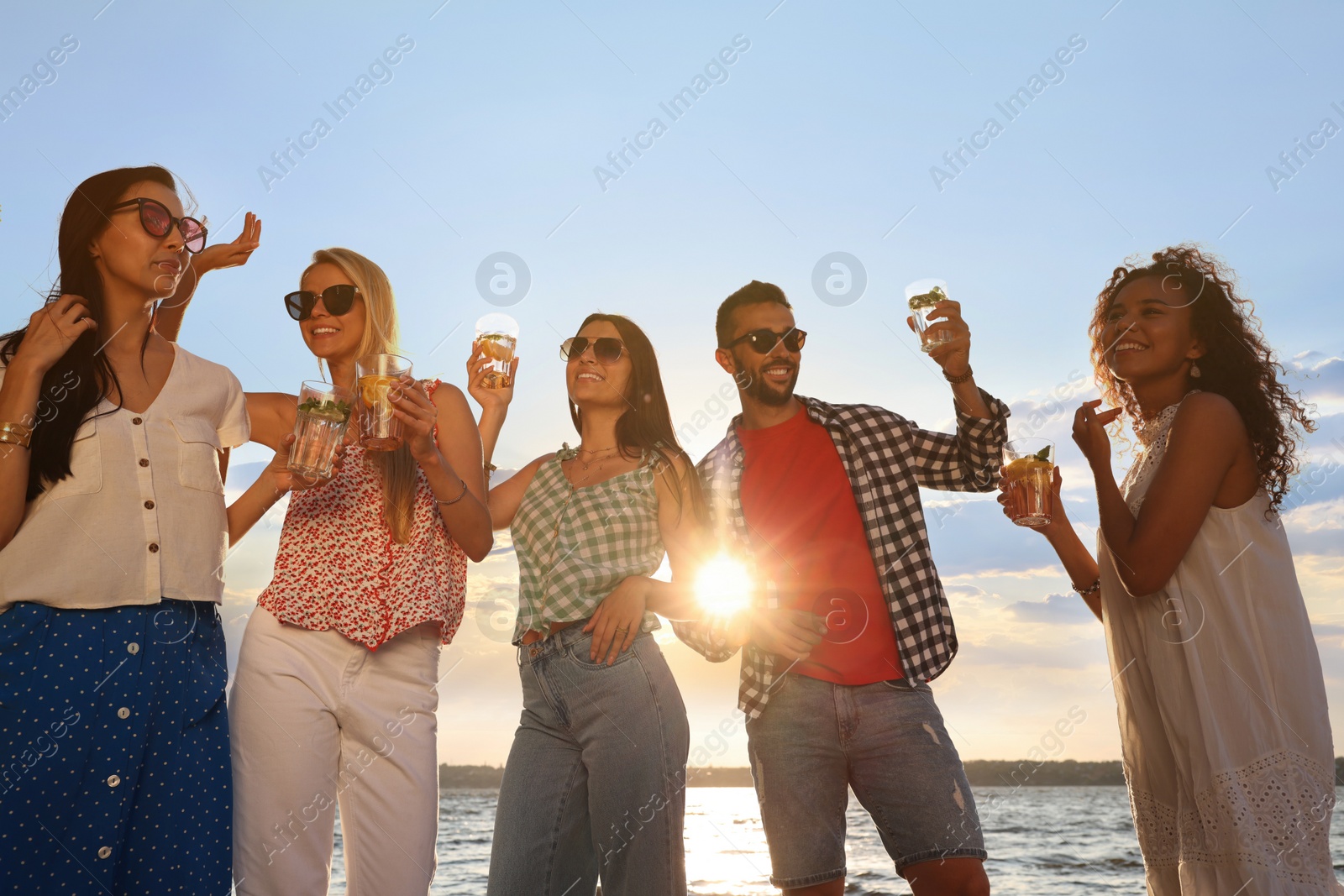 Photo of Group of friends with drinks having fun near river at summer party