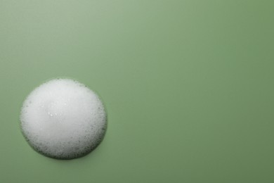 Drop of fluffy soap foam on green background, top view. Space for text