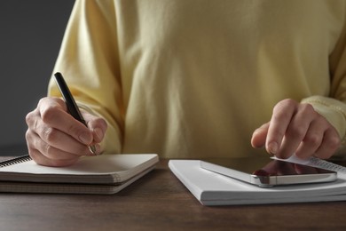 Woman with pen, notepads and smartphone at wooden table, closeup