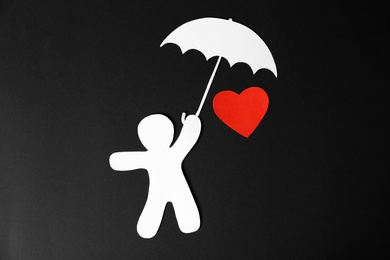 Photo of Paper man with umbrella and red heart on black background, top view