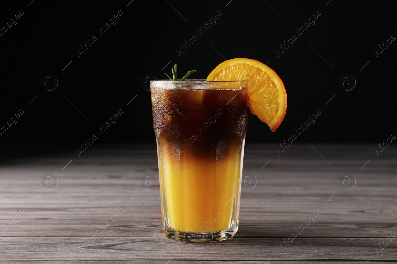 Photo of Tasty refreshing drink with coffee and orange juice on wooden table against dark background