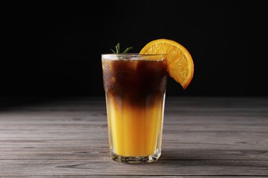 Tasty refreshing drink with coffee and orange juice on wooden table against dark background