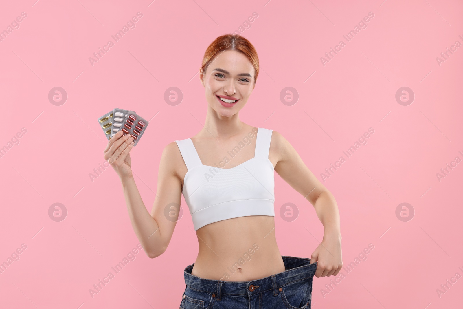 Photo of Slim woman in big jeans with pills on pink background. Weight loss