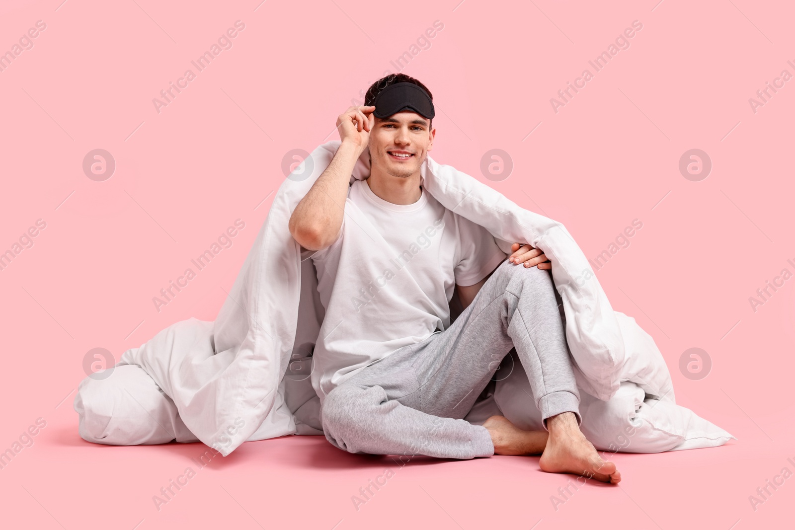 Photo of Happy man in pyjama with sleep mask and blanket on pink background