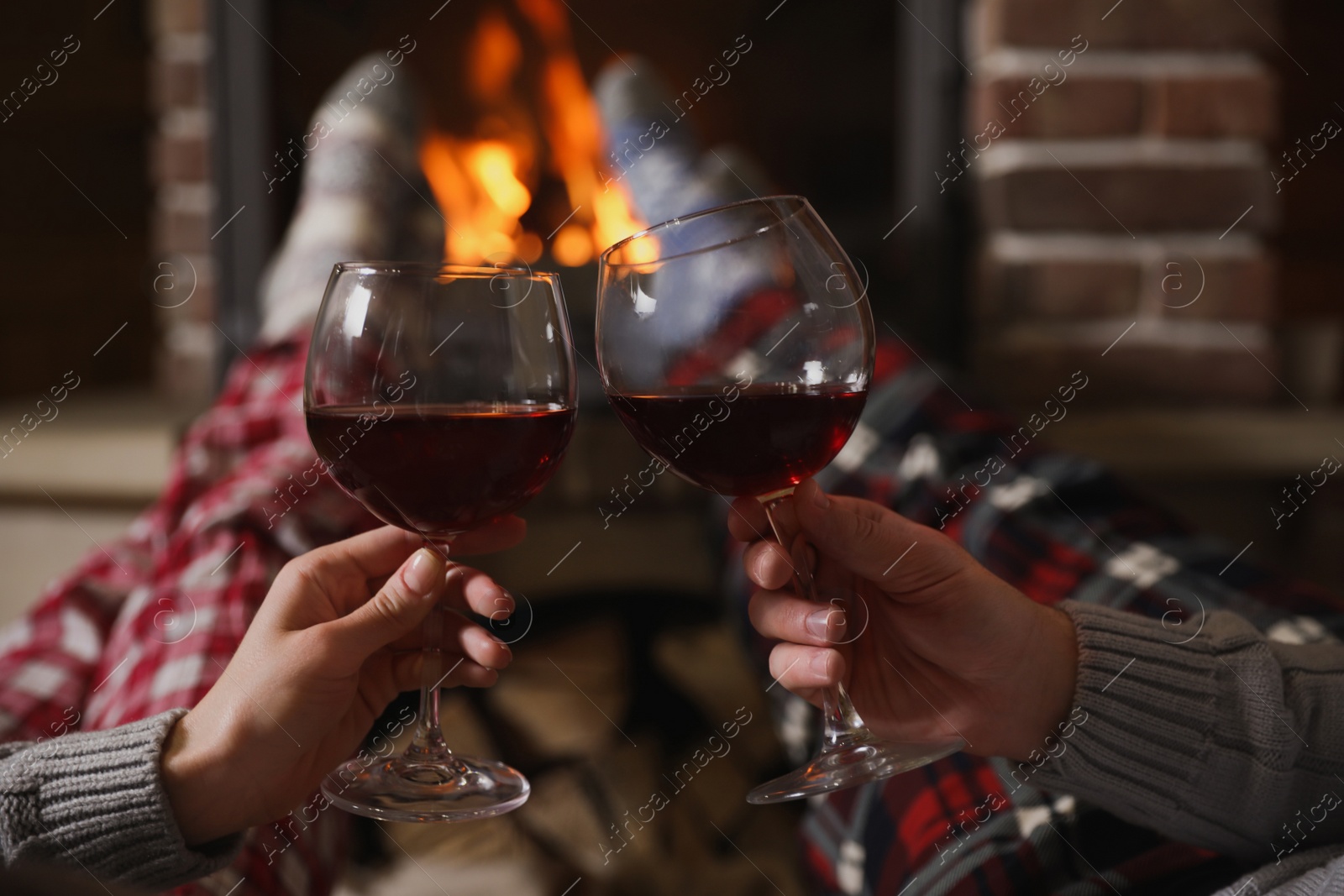 Photo of Couple with glasses of red wine near burning fireplace, closeup