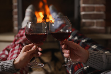 Photo of Couple with glasses of red wine near burning fireplace, closeup