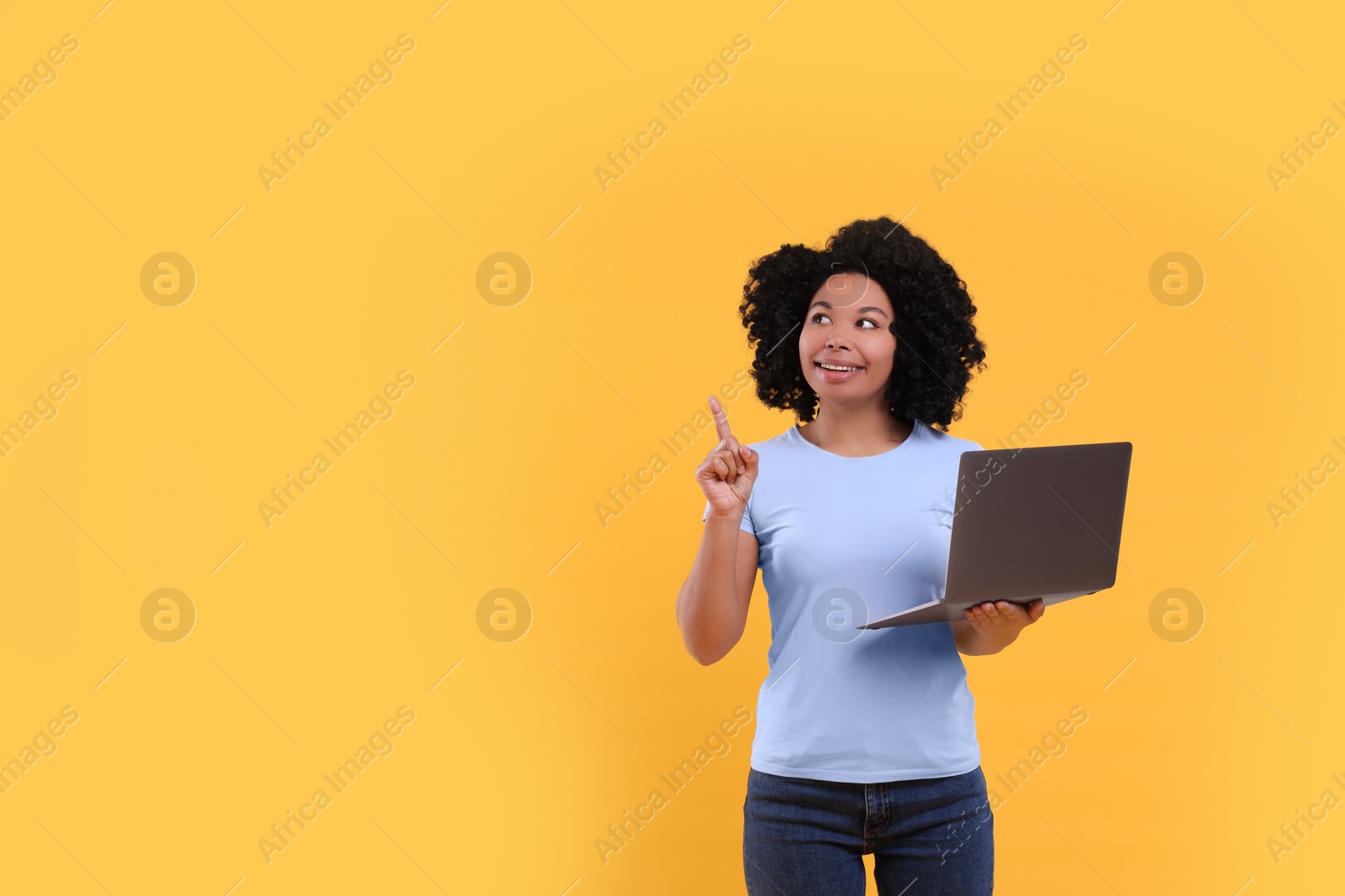 Photo of Happy young woman with laptop pointing at something on yellow background. Space for text