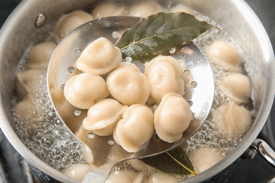 Closeup of dumplings on skimmer over stewpan with boiling water. Home cooking