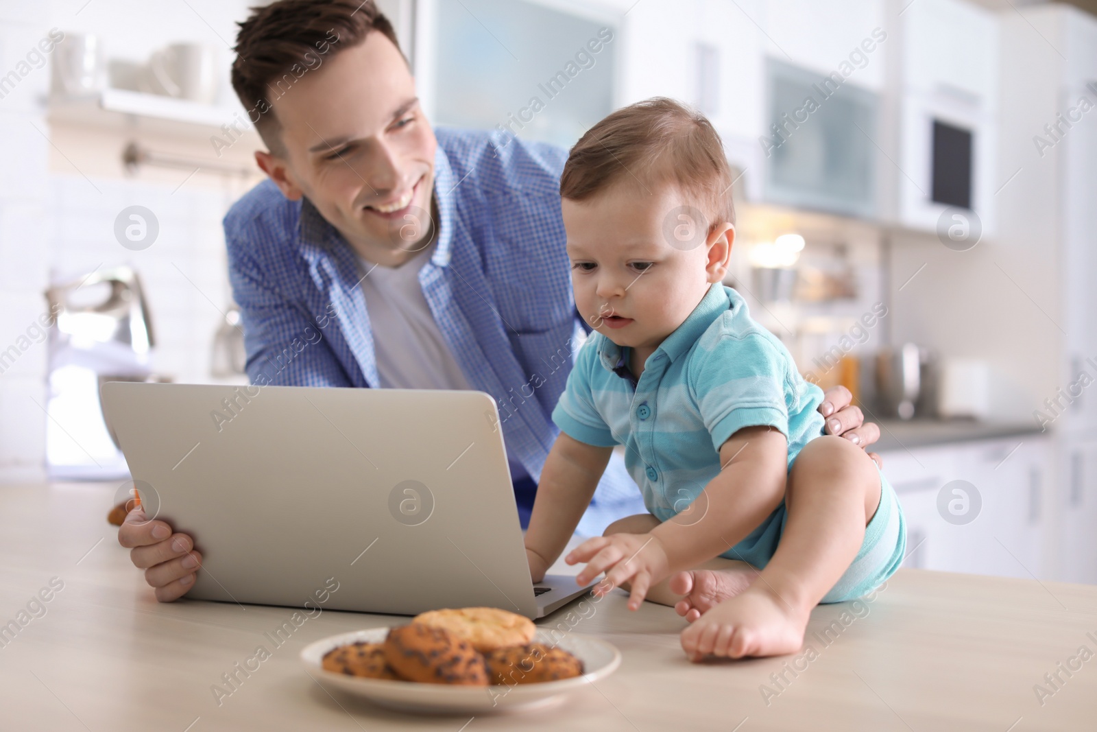 Photo of Young father with his cute little son using laptop in kitchen