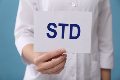 Doctor holding sheet of paper with abbreviation STD on light blue background, closeup