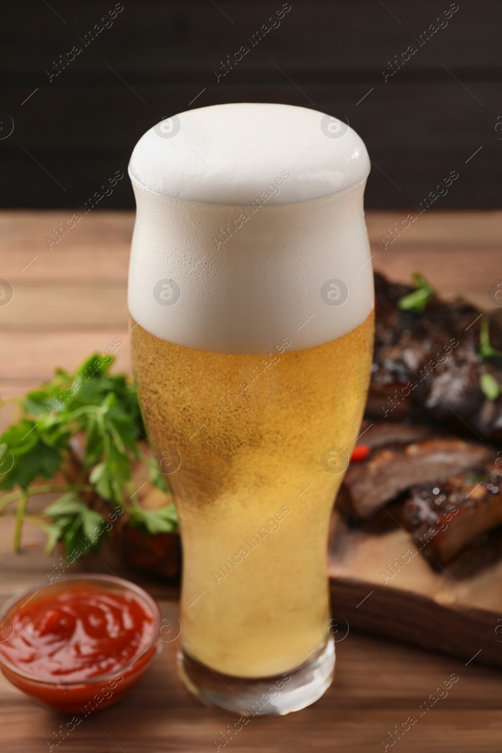 Photo of Glass of beer, tasty grilled ribs and sauce on wooden table