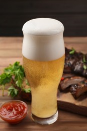 Glass of beer, tasty grilled ribs and sauce on wooden table