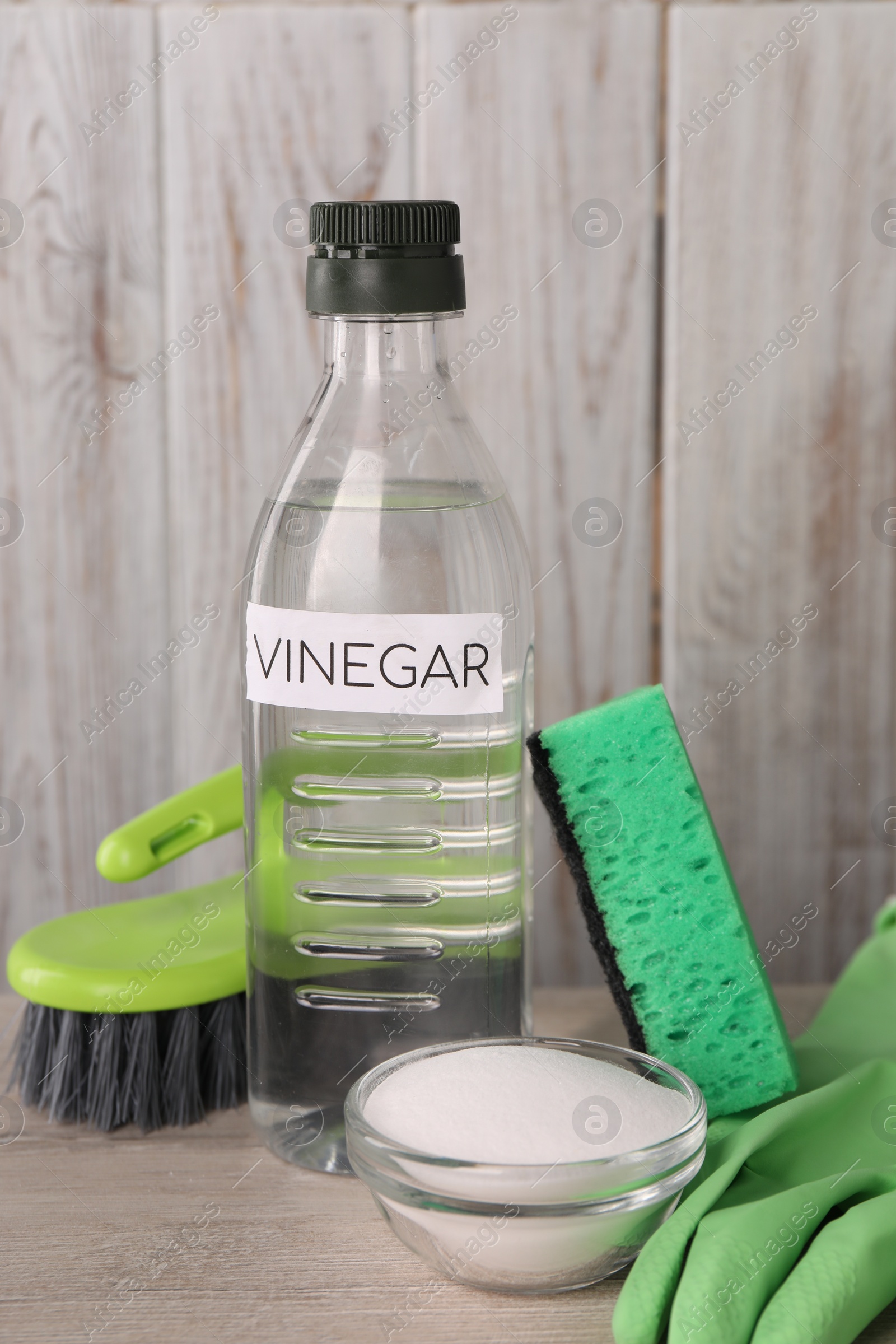 Photo of Natural cleaning products. Vinegar in bottle, baking soda, glove, sponge and brush on light wooden table