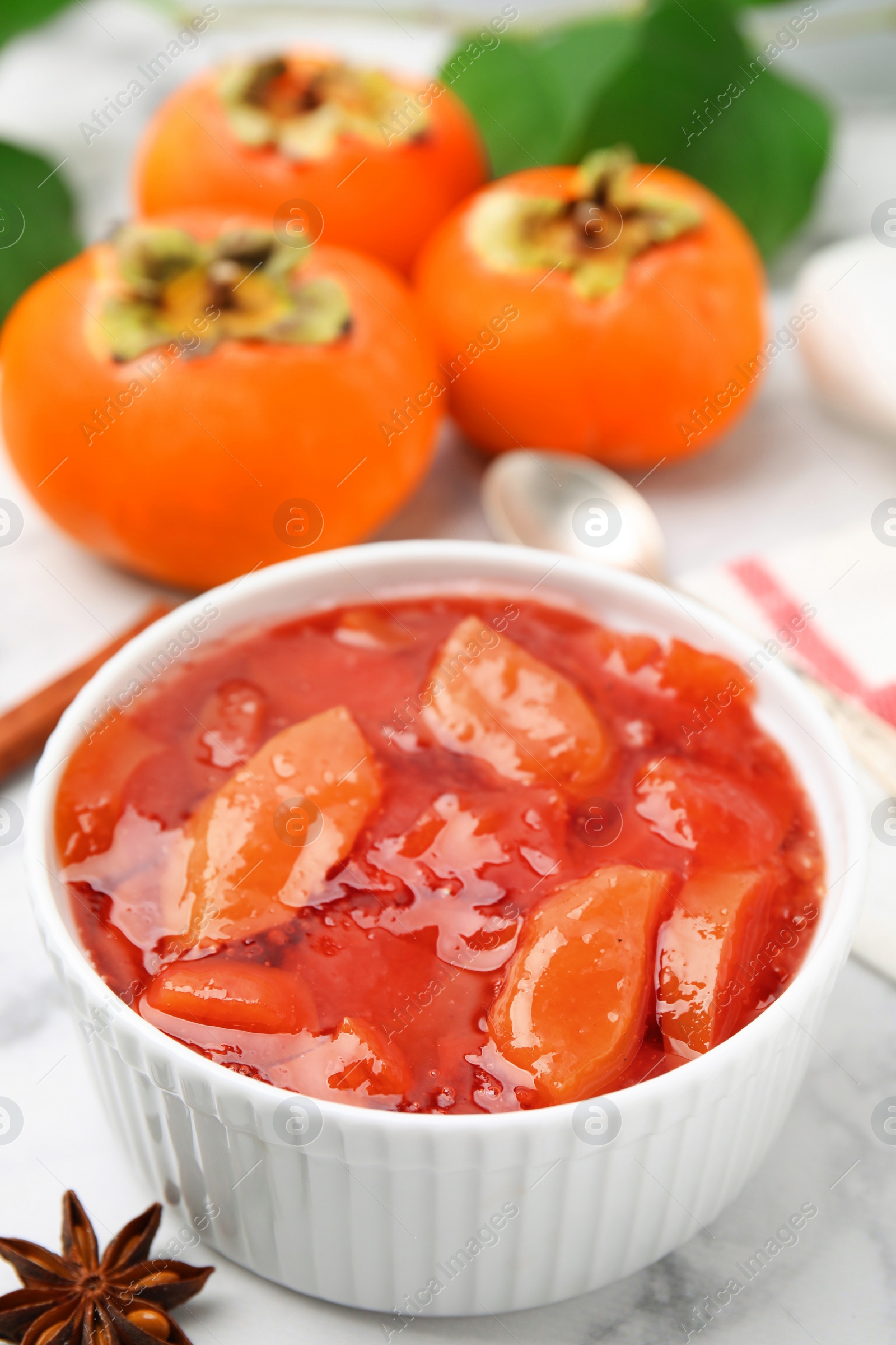 Photo of Bowl of tasty persimmon jam and ingredients on white marble table, above view