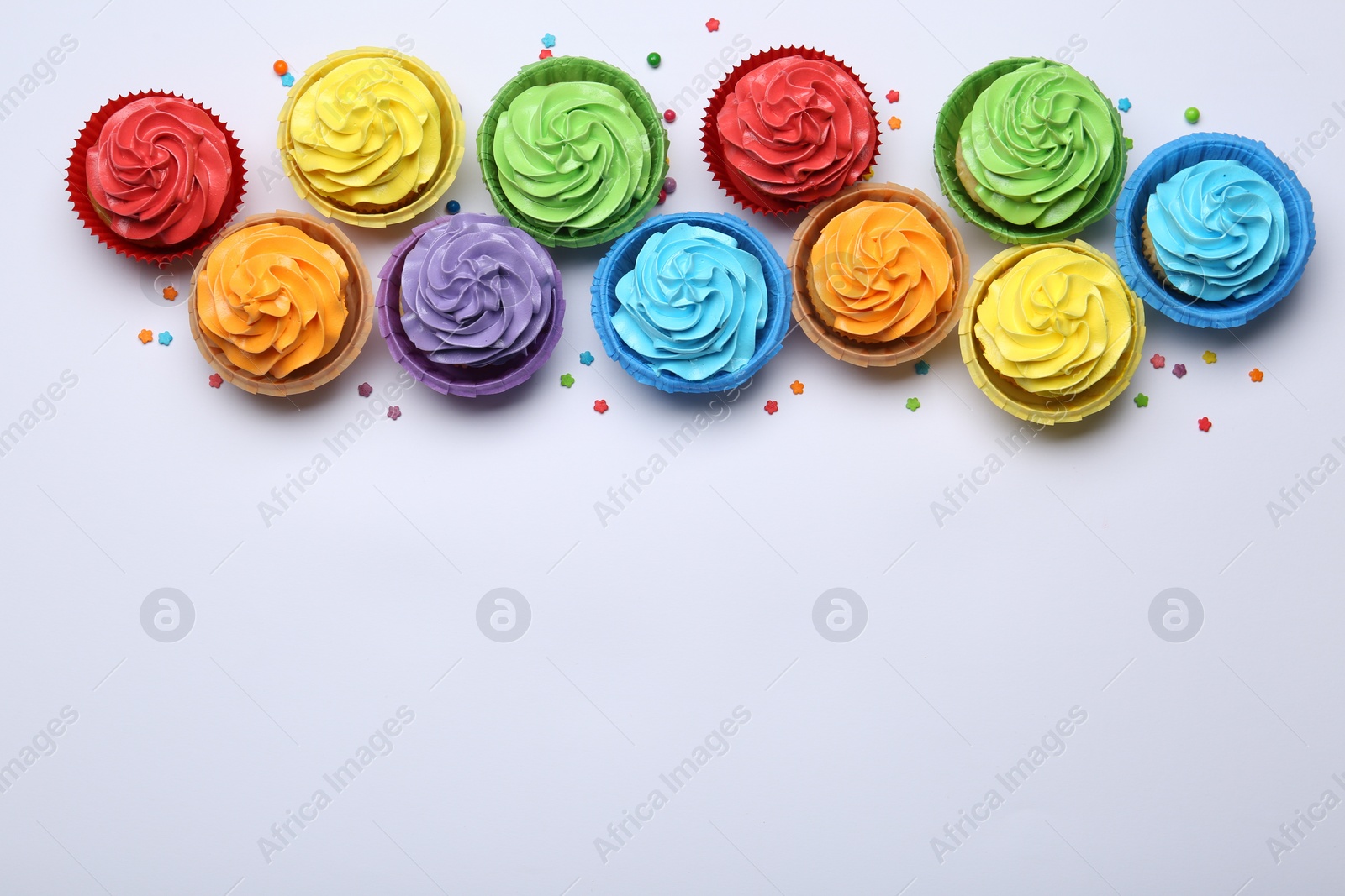 Photo of Many tasty cupcakes with bright cream and sprinkles on white background, flat lay. Space for text