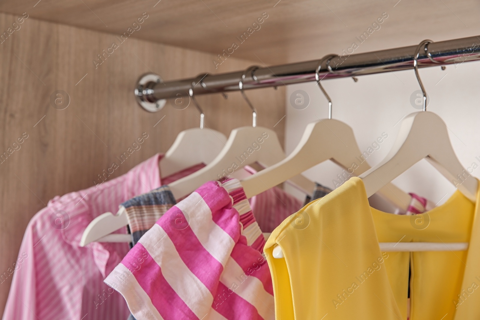 Photo of Stylish girl's clothes hanging in wardrobe, closeup