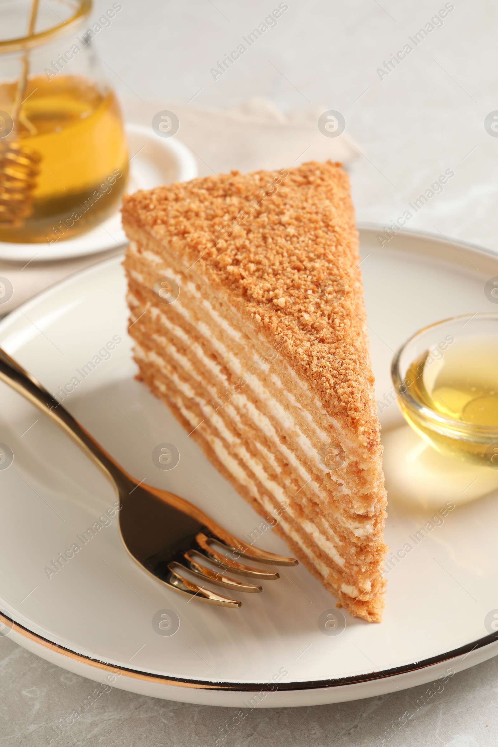 Photo of Slice of delicious layered honey cake served on grey table, closeup