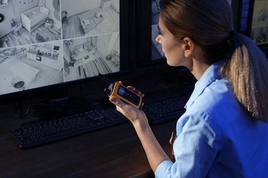 Female security guard with portable transmitter monitoring modern CCTV cameras indoors