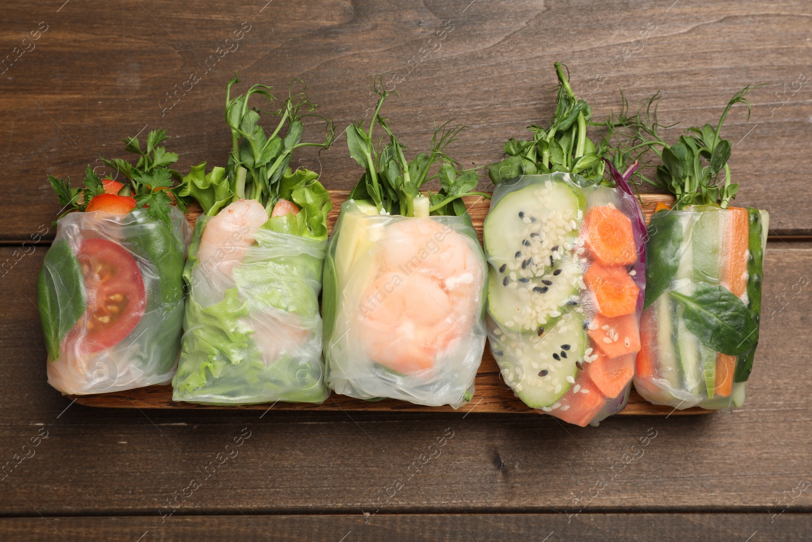 Photo of Many different delicious rolls wrapped in rice paper on wooden table, flat lay