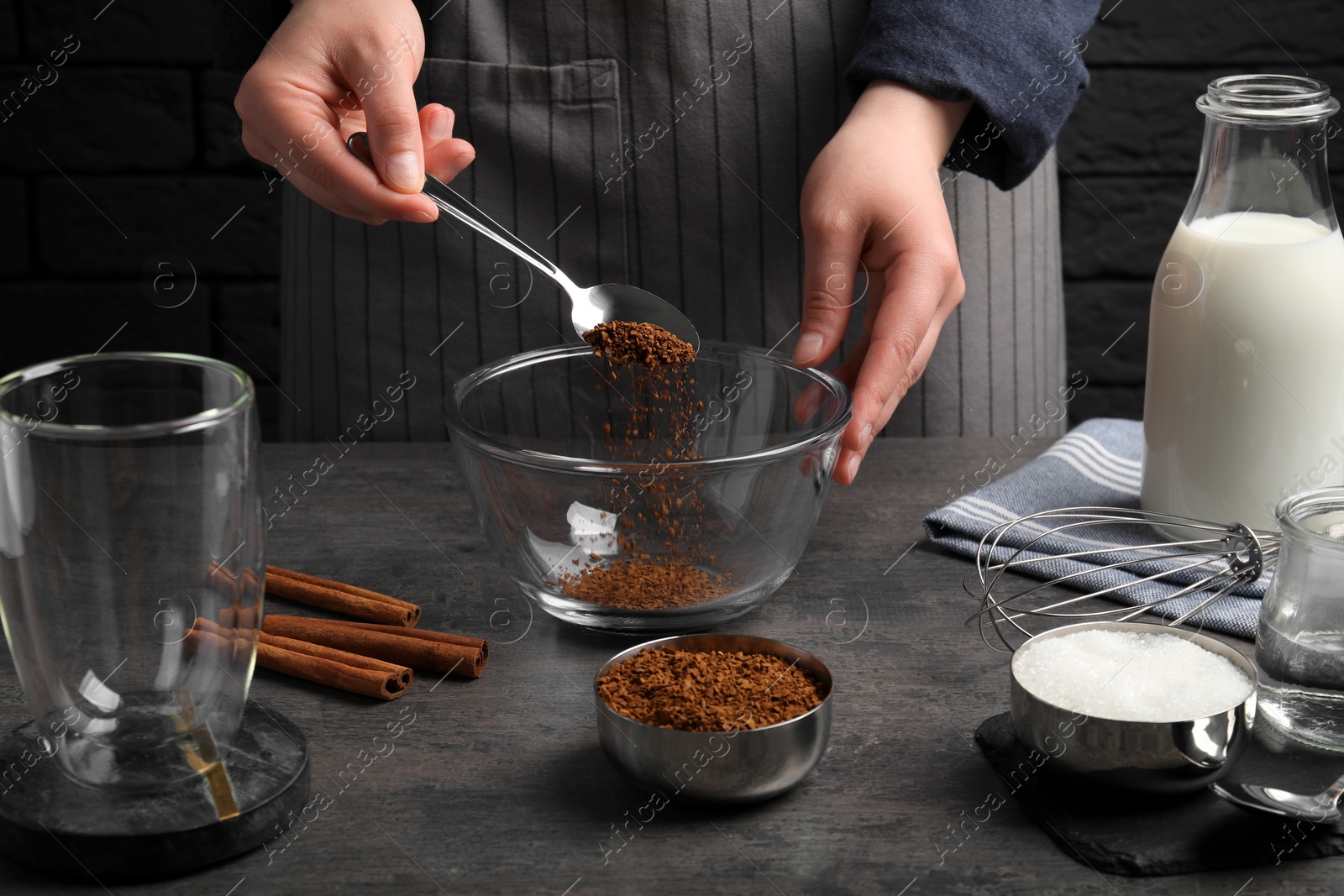 Photo of Making dalgona coffee. Woman pouring instant granules into bowl at grey table, closeup