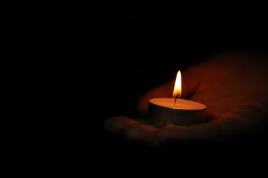 Photo of Woman holding burning candle in darkness, closeup. Space for text