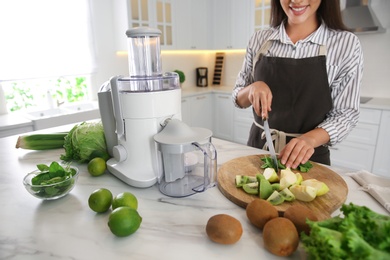 Young woman cutting fresh spinach for juice at table in kitchen, closeup