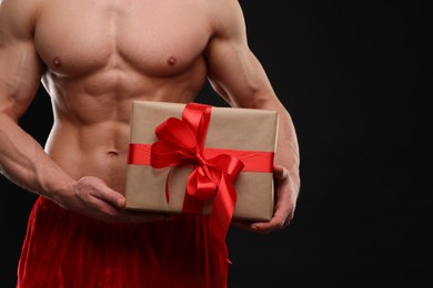 Photo of Attractive young man with muscular body holding Christmas gift box on black background, closeup. Space for text