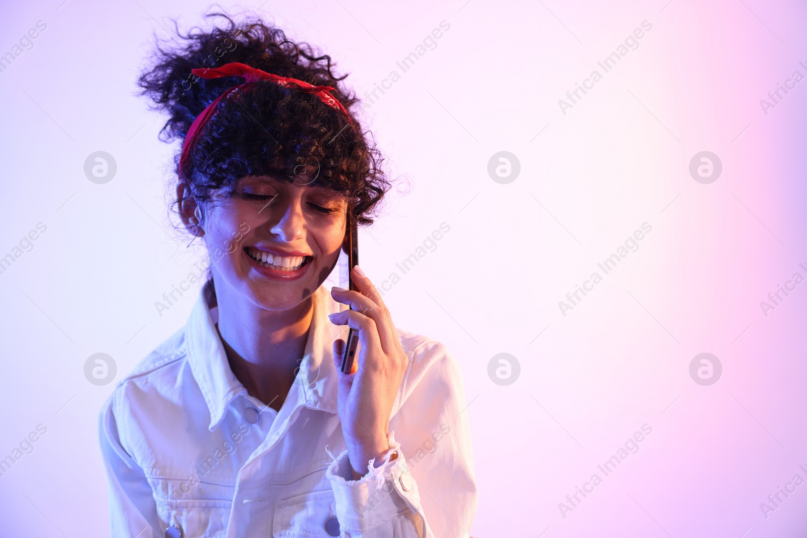 Photo of Beautiful young woman talking on smartphone against color background in neon lights. Space for text