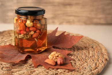 Photo of Different nuts with honey in jar and dry leaf on table. Space for text