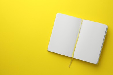 Photo of Open notebook with blank pages on yellow background, top view. Space for text