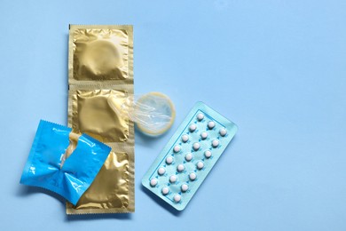 Condoms and contraception pills on light blue background, flat lay and space for text. Choosing birth control method