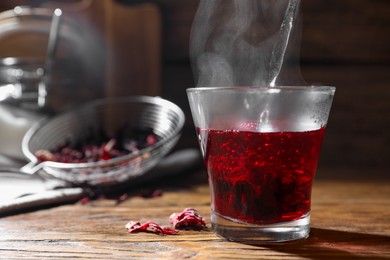 Photo of Making hibiscus tea. Pouring hot water into cup with roselle petals at wooden table, closeup. Space for text