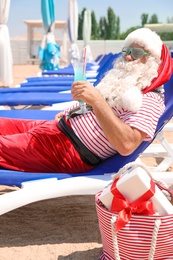 Photo of Authentic Santa Claus with cocktail resting on lounge chair at resort